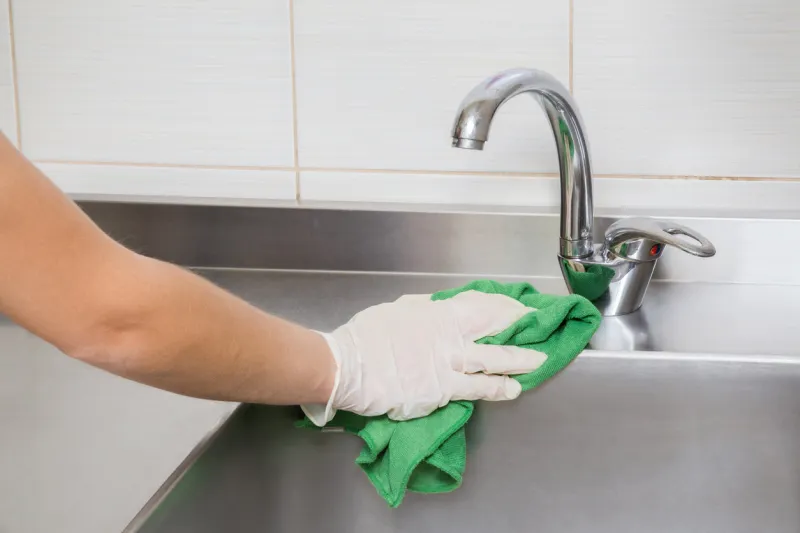 hand in protective glove with rag cleaning kitchen equipment in the professional kitchen stainless steel sink early spring cleaning or regular clean up