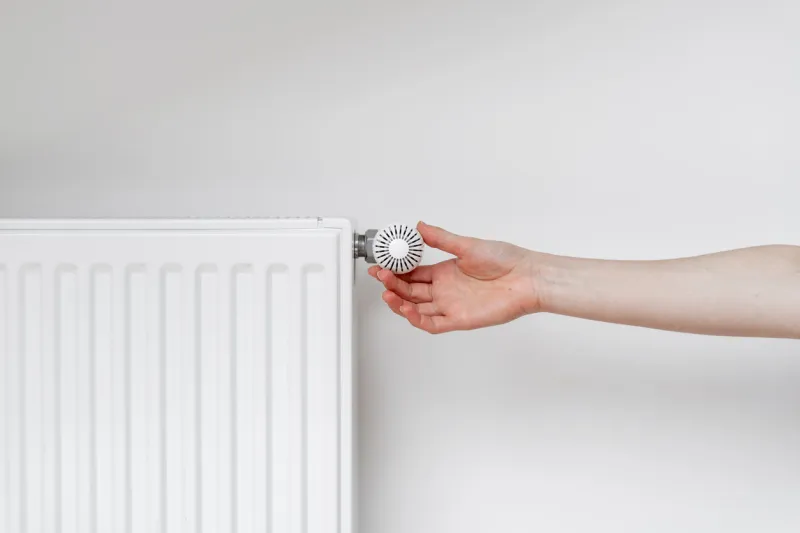 cropped view of woman hand adjusting thermostat on white heating radiator consumption of natural resource, saving energy and warm home concept