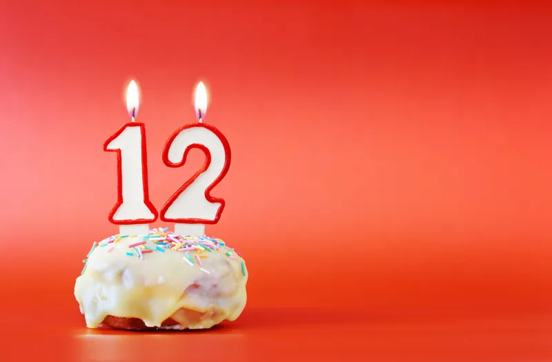twelve years birthday cupcake with white burning candle in the form of number 12 vivid red background with copy space