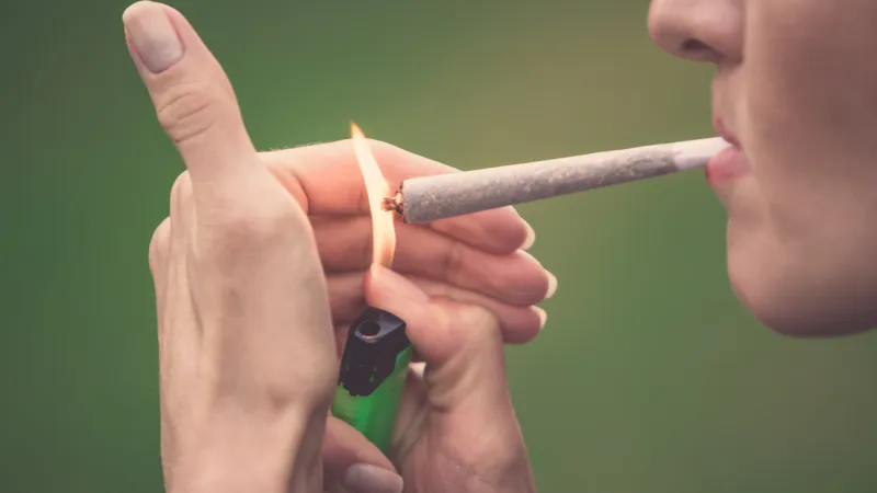 close-up of woman lighting up marijuana cannabis joint with lighter and big fire ready made marihuana hashish cigarette bought in coffee shop of amsterdam (holland - netherlands)