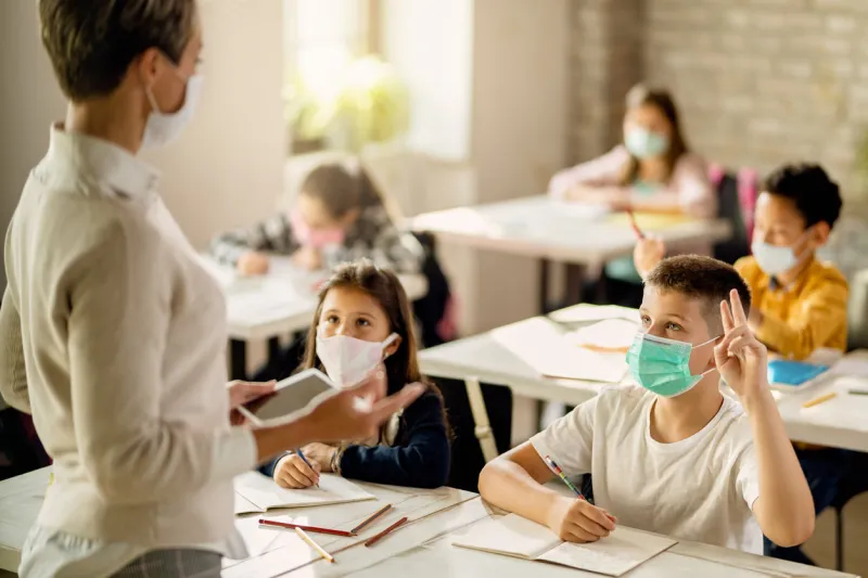 schoolboy with face mask raising hand to answer the question during a class in the classroom