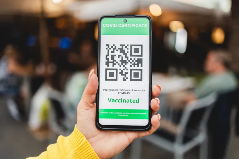 hand holding digital green pass certificate for coronavirus vaccine with bar restaurant on background