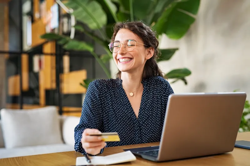 young happy woman doing shopping online with her laptop at home portrait of excited woman holding credit card and buy on an e-commerce site with copy space beautiful laughing girl paying online bills using debit card and computer