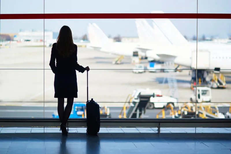 young woman in the airport, looking through the window at planes