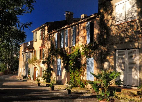 trees giving shade to sun lit mediterranean house facades in gassin provence france on a beautiful autumn day with a clear blue sky