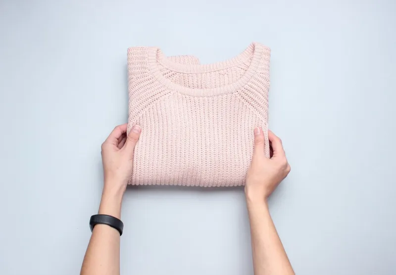 hands fold knitted sweater on a gray background conceptual photo top view