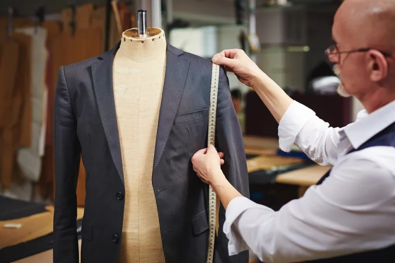 tailor with measuring tape taking measures of jacket on mannequin