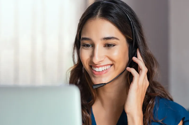 smiling woman using laptop while talking to customer on phone consulting corporate client in conversation with customer using computer on desk service desk consultant talking in a call center and working on laptop