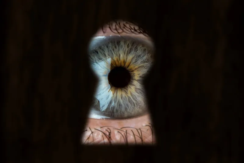 female blue eye looking through the keyhole the concept of voyeurism, curiosity, stalker, surveillance and security