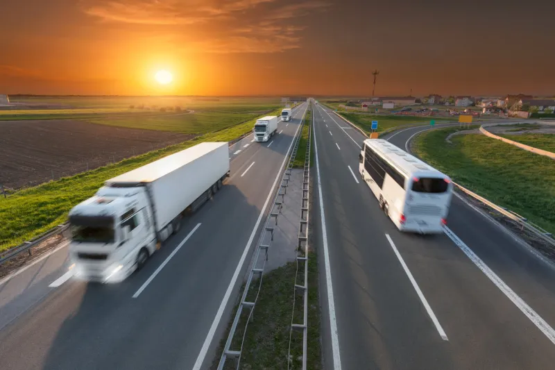 many white trucks in line and fast travel bus driving towards the sun speed blurred motion drive on the freeway at beautiful sunset transport travel scene on the motorway near belgrade, serbia