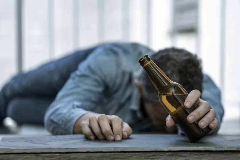 drunk man lying on the floor asleep with a bottle of beer in his hand alcohol consumption addiction alcoholism concept focus selected
