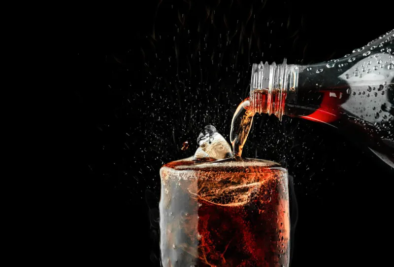 pour soft drink in glass with ice splash on dark background