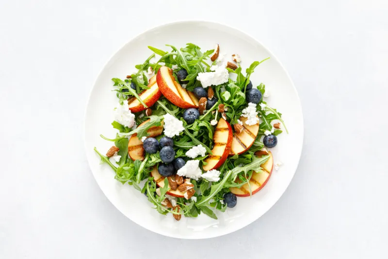 peach, blueberry and arugula fresh fruit salad with cheese and almond nuts, top view