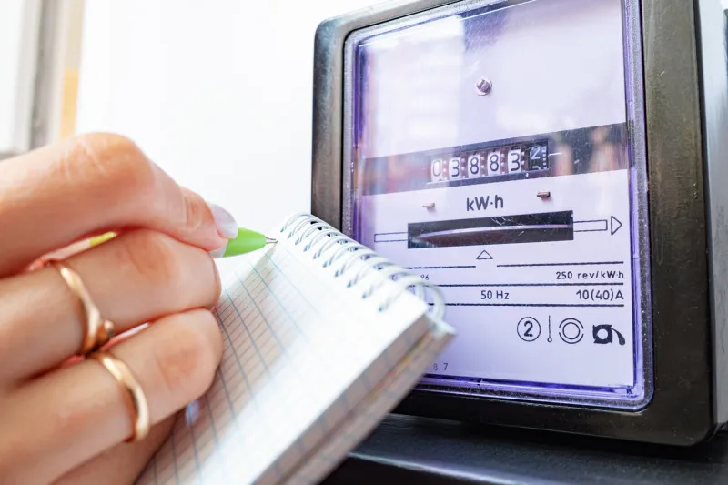 woman's hands with pen and notepad writes the electricity meter readings at home