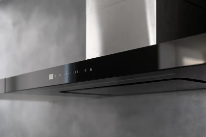 state of art sleek technological black exhaust hood, touch controls marked with white, kitchen appliance in apartment with modern interior, light grey wall in blurred background close up shot