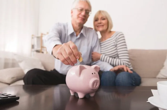 senior couple putting coin in piggybank, saving money at home