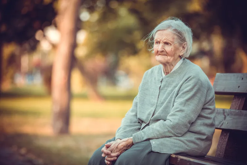 portrait of senior woman sitting on bench in autumn park old lady feeling lonely and sad frustrated aged female outdoors
