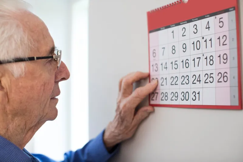 confused senior man with dementia looking at wall calendar