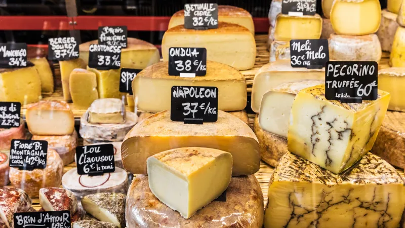 a large selection of different french and italian cheeses on the counter of a small store at the market in the bastille district paris, france