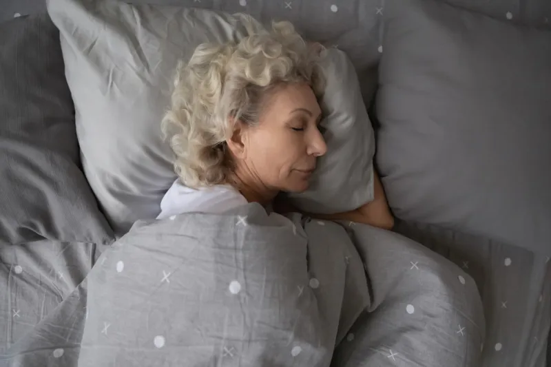top view of peaceful elderly woman sleep relax in comfortable home bed, rest on cozy soft fluffy pillow, under warm blanket, calm senior female rest take nap in cozy bedroom, relaxation concept