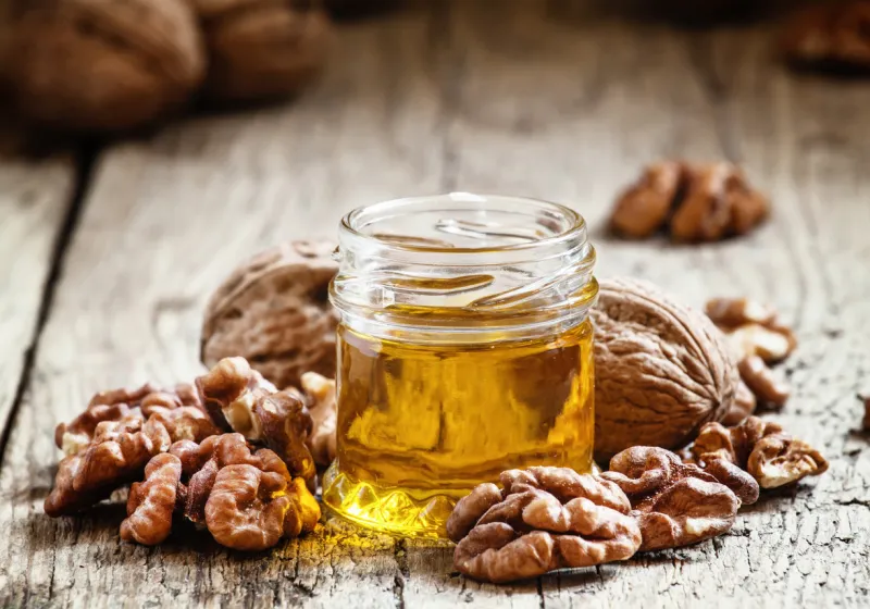 walnut oil in a small jar and kernels on old wooden background in rustic style, selective focus