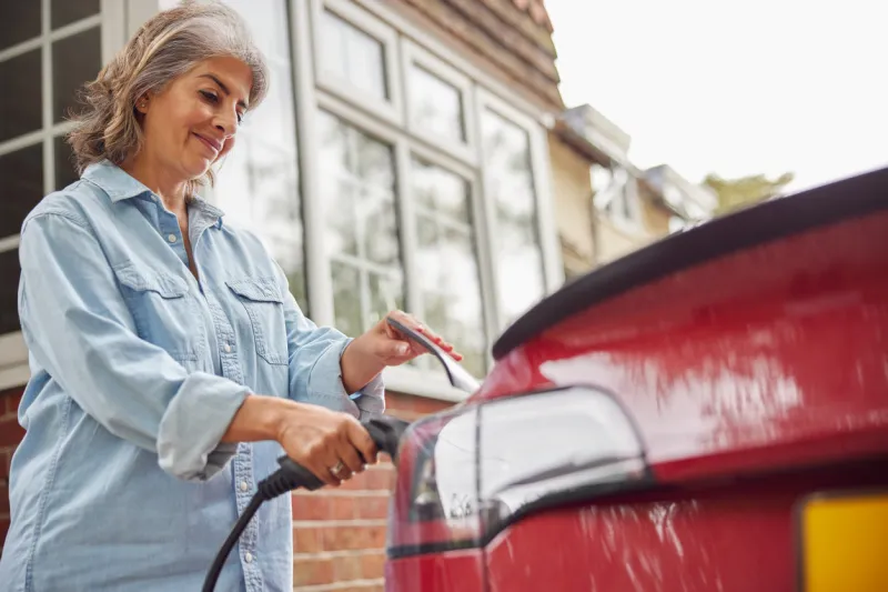 mature woman attaching charging cable to environmentally friendly zero emission electric car at home