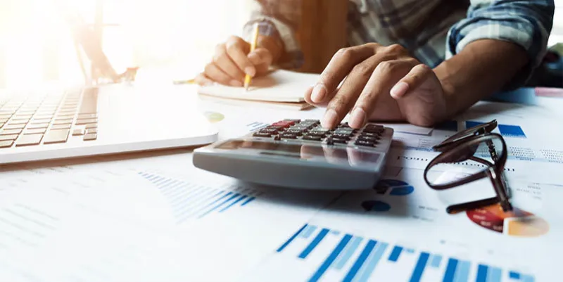 close up of businessman or accountant hand holding pen working on calculator and laptop computer to calculate business data during make note at notepad, accountancy document at office, business financial concept