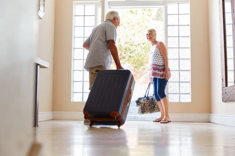senior couple standing by front door with suitcase about to leave for vacation
