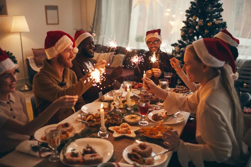 multi-ethnic group of people holding sparklers while enjoying christmas dinner at home