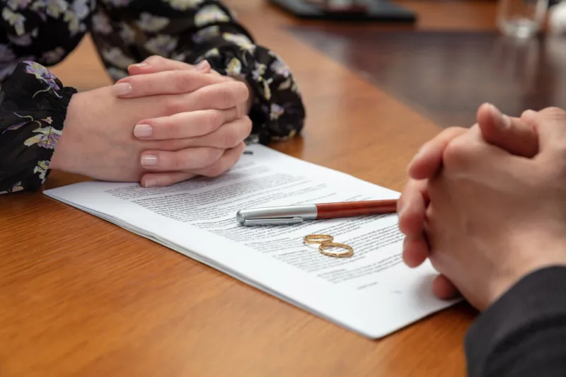 signing a divorce, marriage dissolution documents and agreement wife and husband hands, wedding rings and legal papers for signature on a wooden table, lawyer office