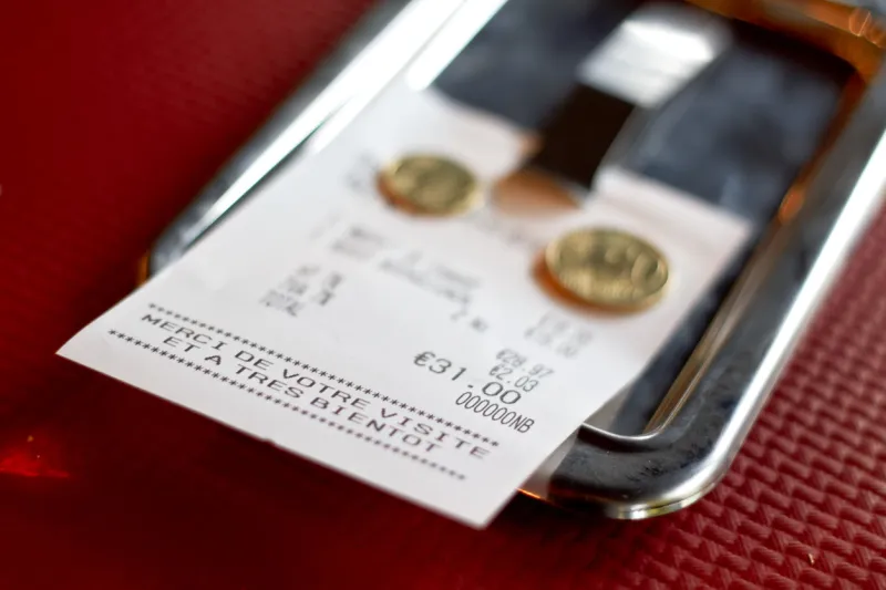 european (french) restaurant check with few tip coins left on it red paper napkin background, selective focus
