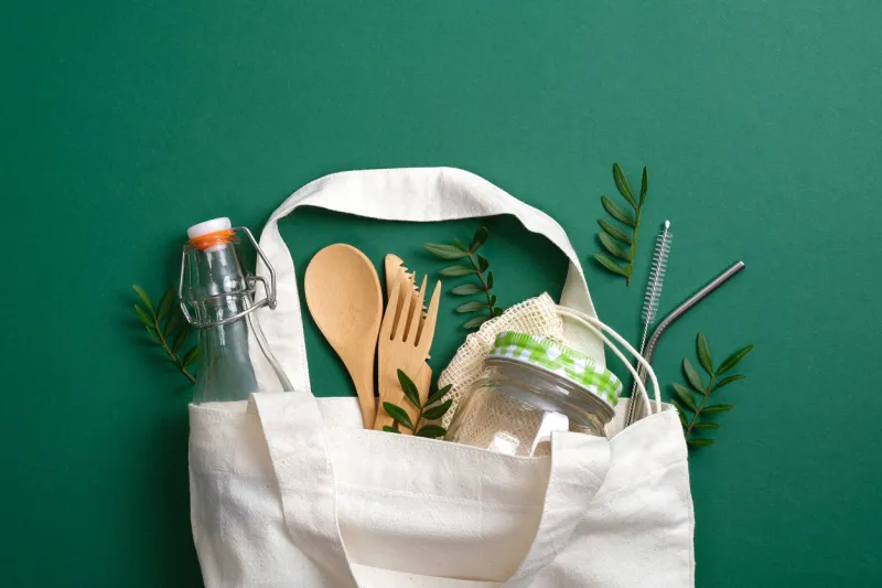 reusable canvas shopper bag with eco friendly bamboo cutlery, metal drinking straws, glass jar and bottle zero waste, plastic free concept sustainable lifestyle