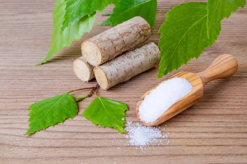 sugar substitute xylitol, a scoop with birch sugar, liefs and wood on wooden background