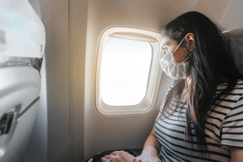 young woman with protection mask is sitting in airplane and watching the view from window corona virus outbreaking high quality photo