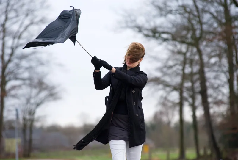 a young woman is fighting against the storm with her umbrella