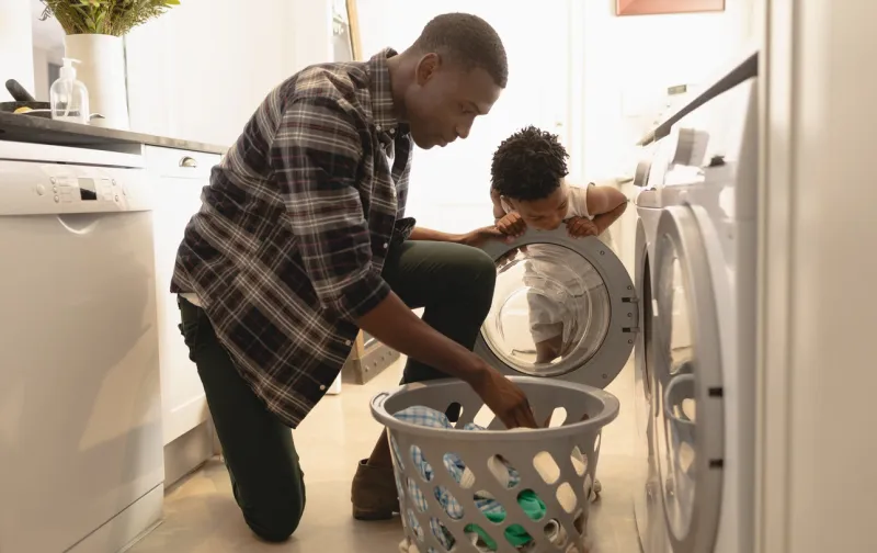 african american father and son washing clothes in washing machine at home