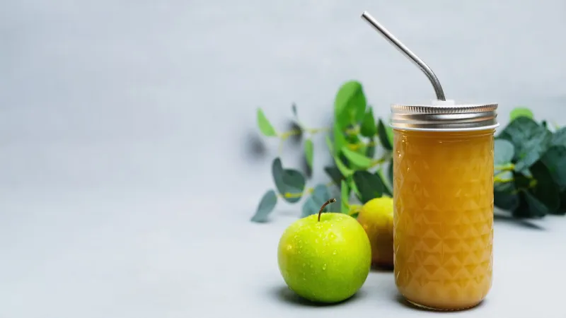 fresh squeezed apple juice with pulp or fruit smoothie apple drink in glass with metal straw on grey background, copy space dietary beverage, healthy drink and dieting concept