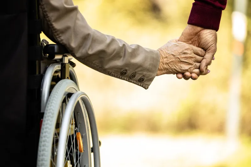 elderly people in wheelchair holding hands together