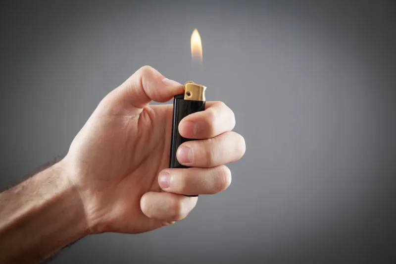 male hand burning lighter in grey background
