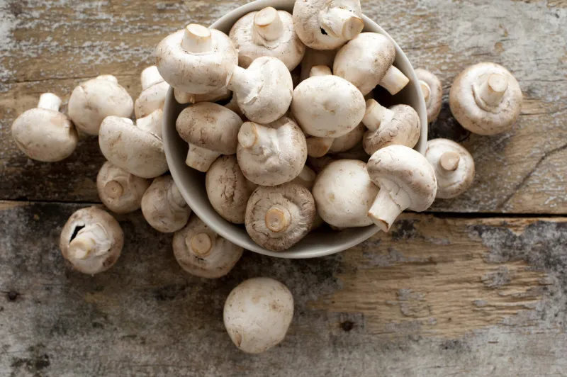 fresh whole white button mushrooms, or agaricus, in a bowl on a rustic wooden counter ready to be cleaned and washed for dinner, overhead view