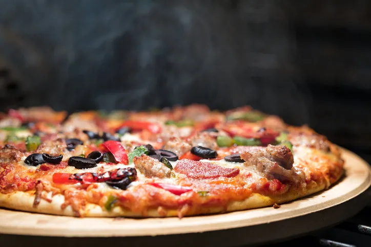 hot supreme thin crust pizza cooking in oven with steam and smoke