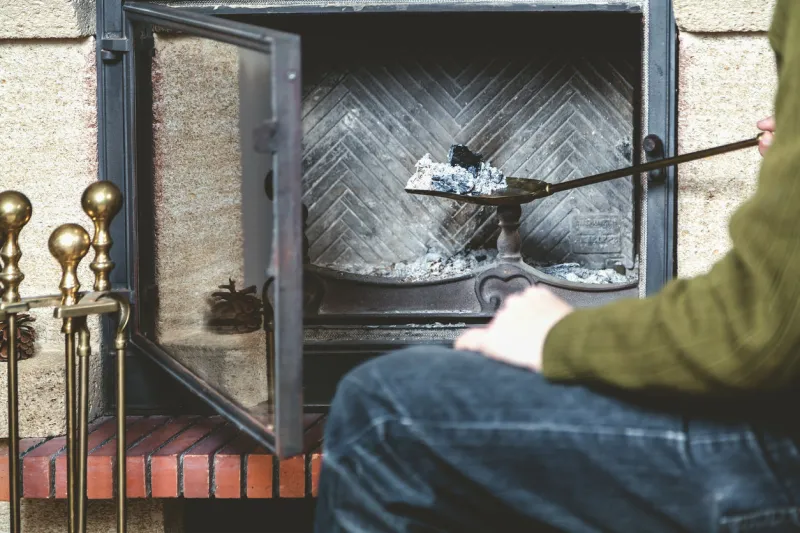 a man cleans the fireplace taken out of the fire a long-handled shovel with ash