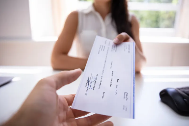 close-up of a businesswoman's hand giving cheque to colleague