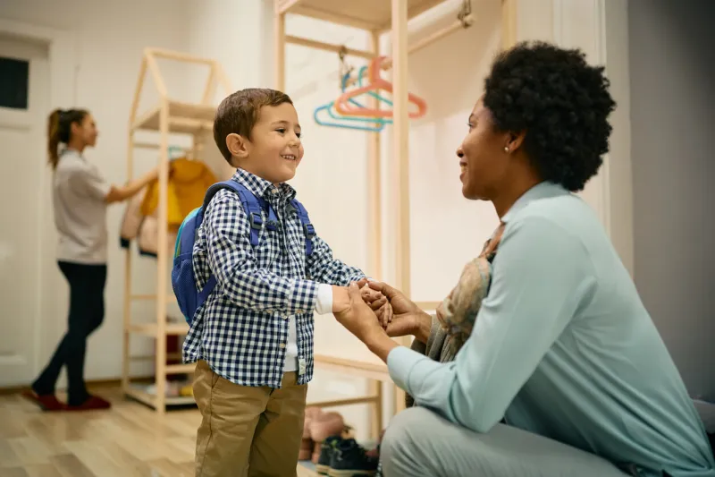 happy african american mother holding hands with her adopted son while greeting him on his first day at preschool