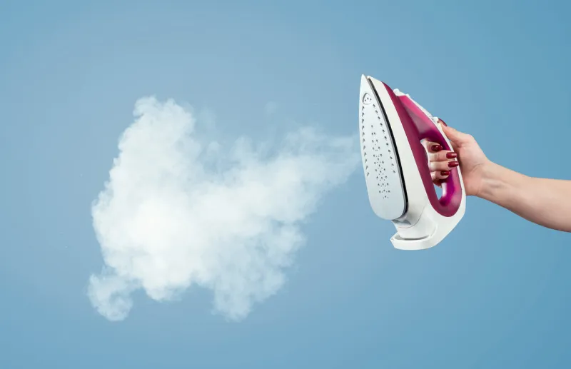 female hand holds the iron with steam on a blue background