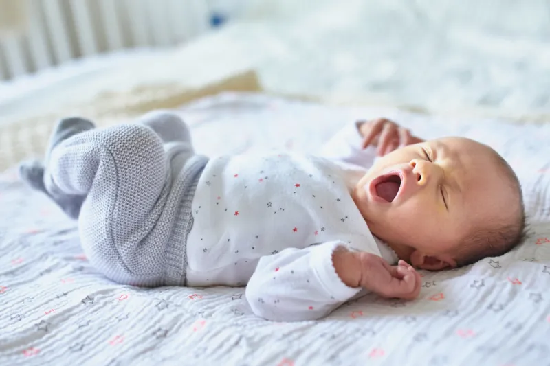 adorable newborn baby girl sleeping and yawning in bed at home