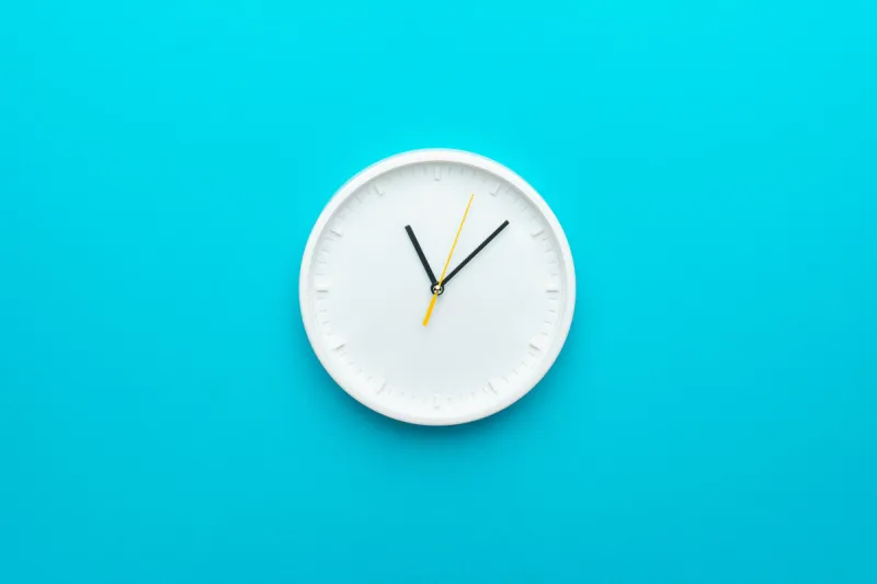 white wall clock with yellow second hand hanging on the wall minimalist flat lay image of plastic wall clock over blue turquiose background with copy space and central composition