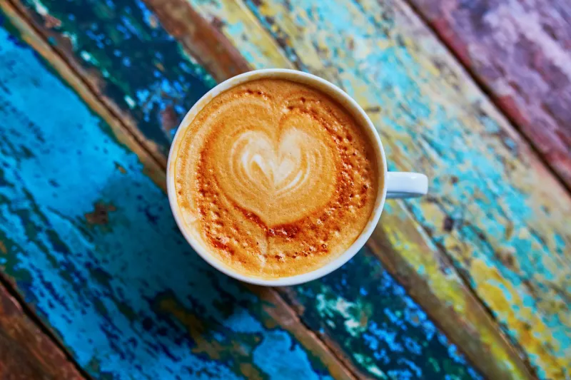 cup of fresh coffee with heart form milk drawing on blue wooden table, view from above, flat lay