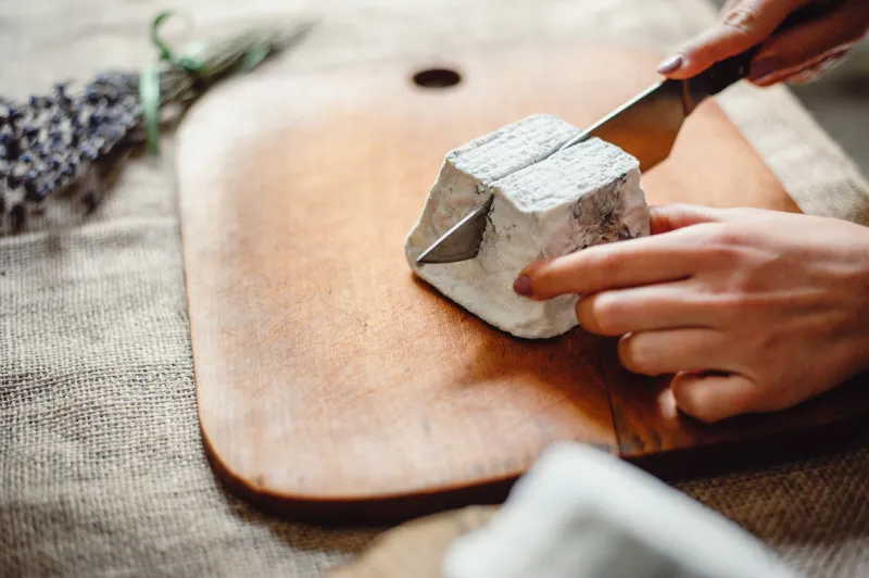valencay cheese on a wooden board cheesemaker cuts cheese with blue mold, close-up french soft cheese from goat's milk cheese composition copy space place for text