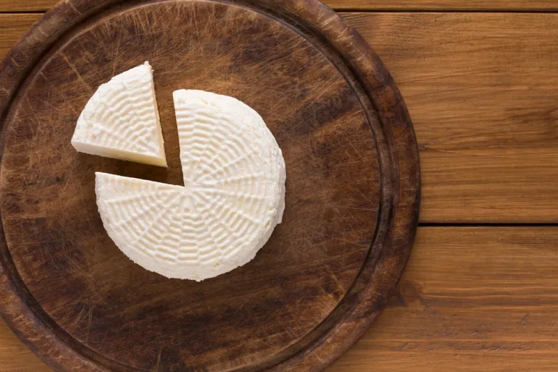 cheese wheel, fresh homemade indian paneer on wooden board, top view with copy space
